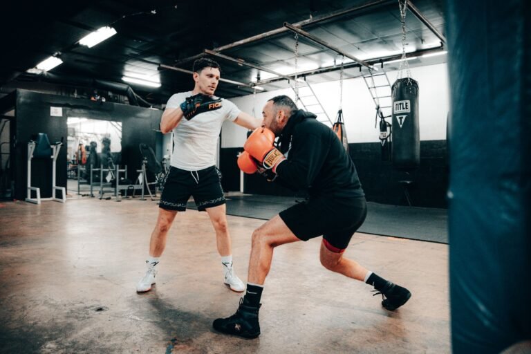 Two men engaged in a dynamic boxing training session indoors, showcasing fitness and athleticism.